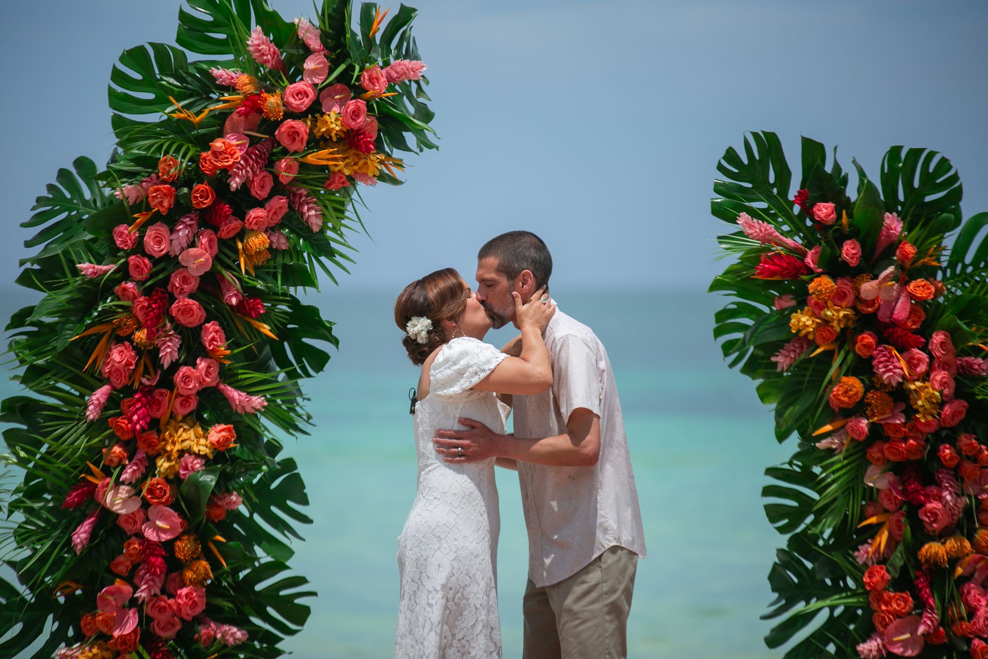 bride and groom kissing in between flowers on the beach