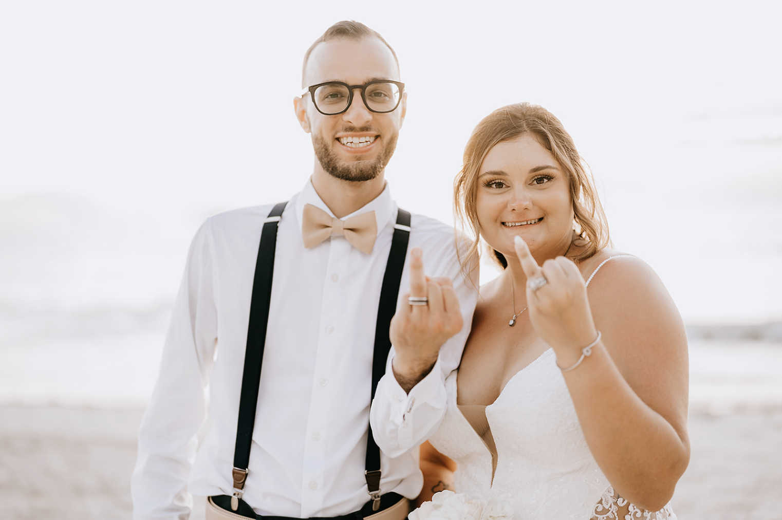 bride and groom on the beach showing their wedding rings